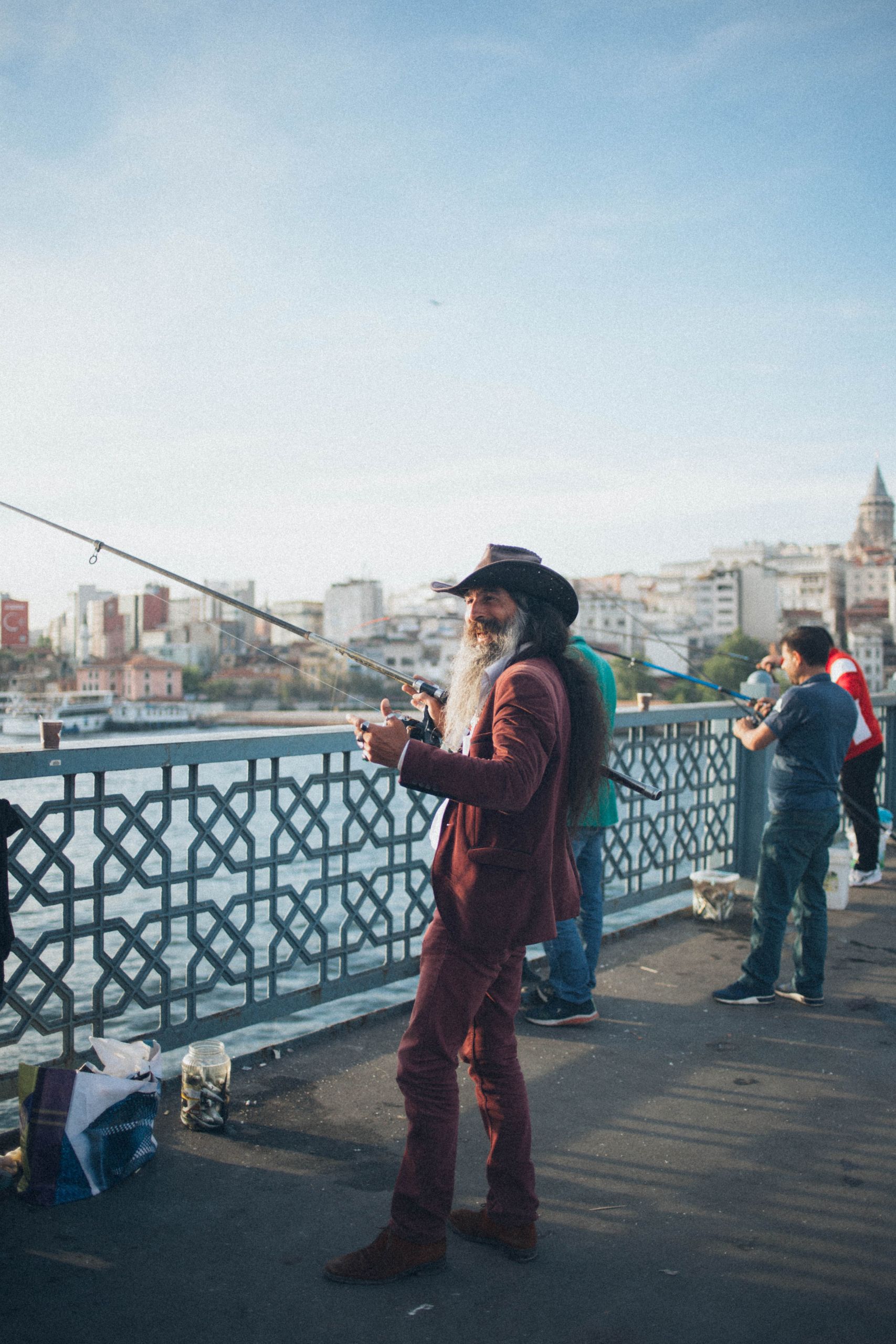 A man in a cowboy hat and red suit fishing on the bridge.
