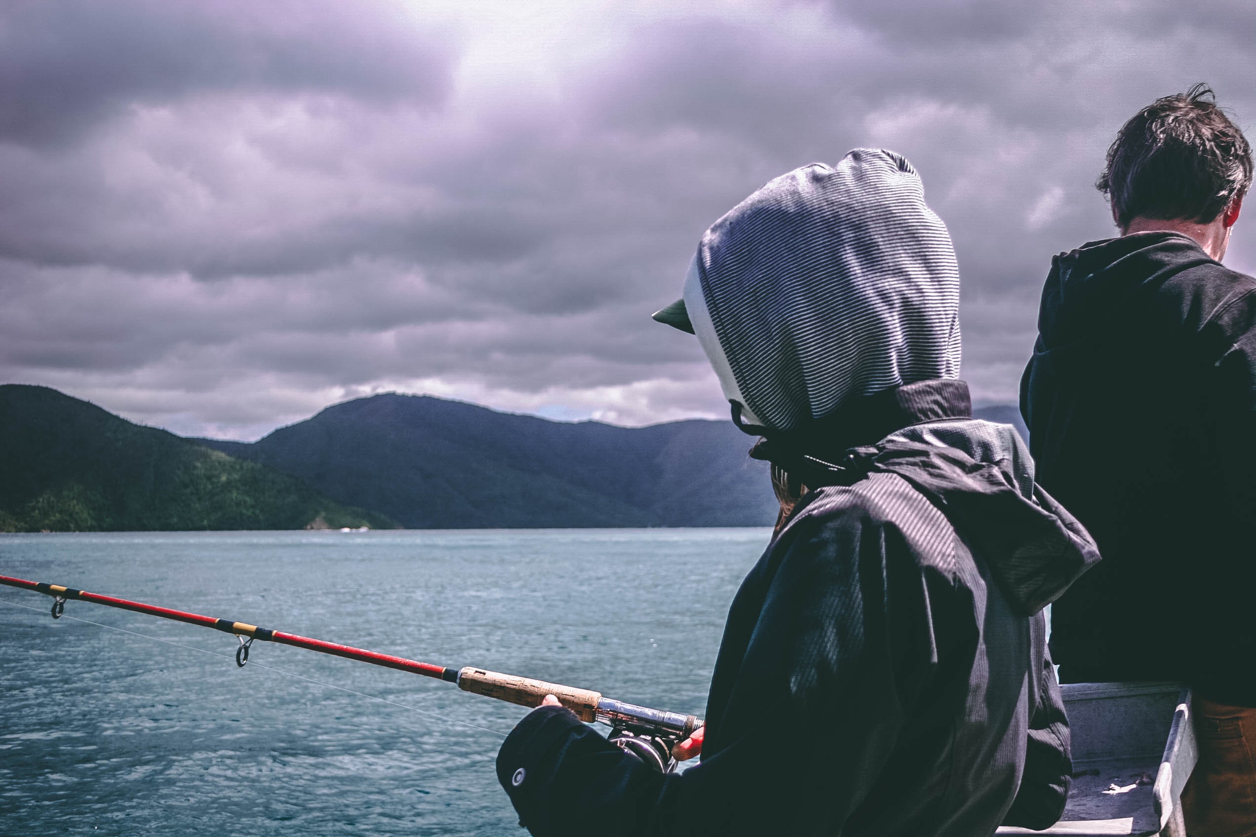 A person in a hooded jacket fishing on the water.