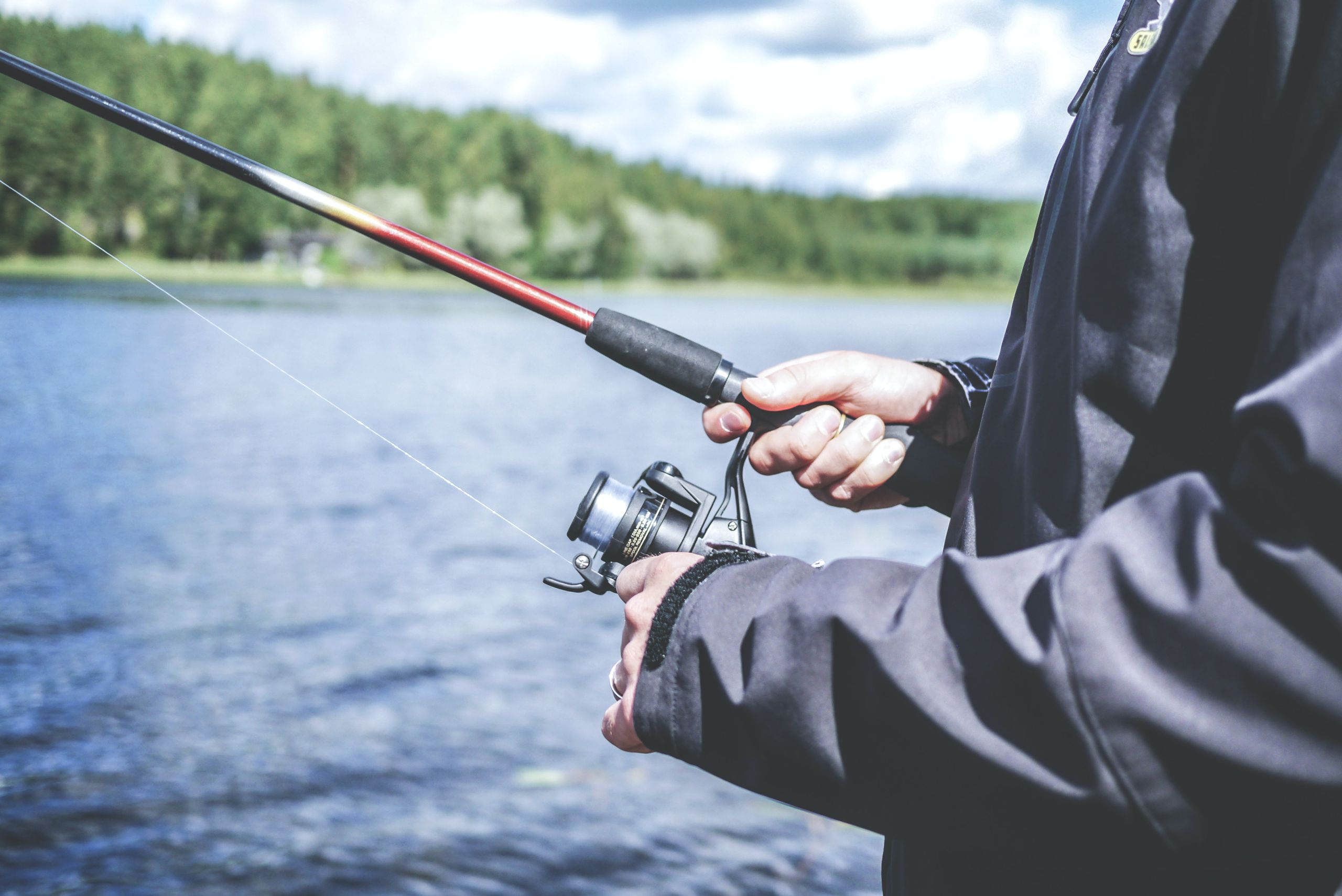 A person holding a fishing rod in front of water.