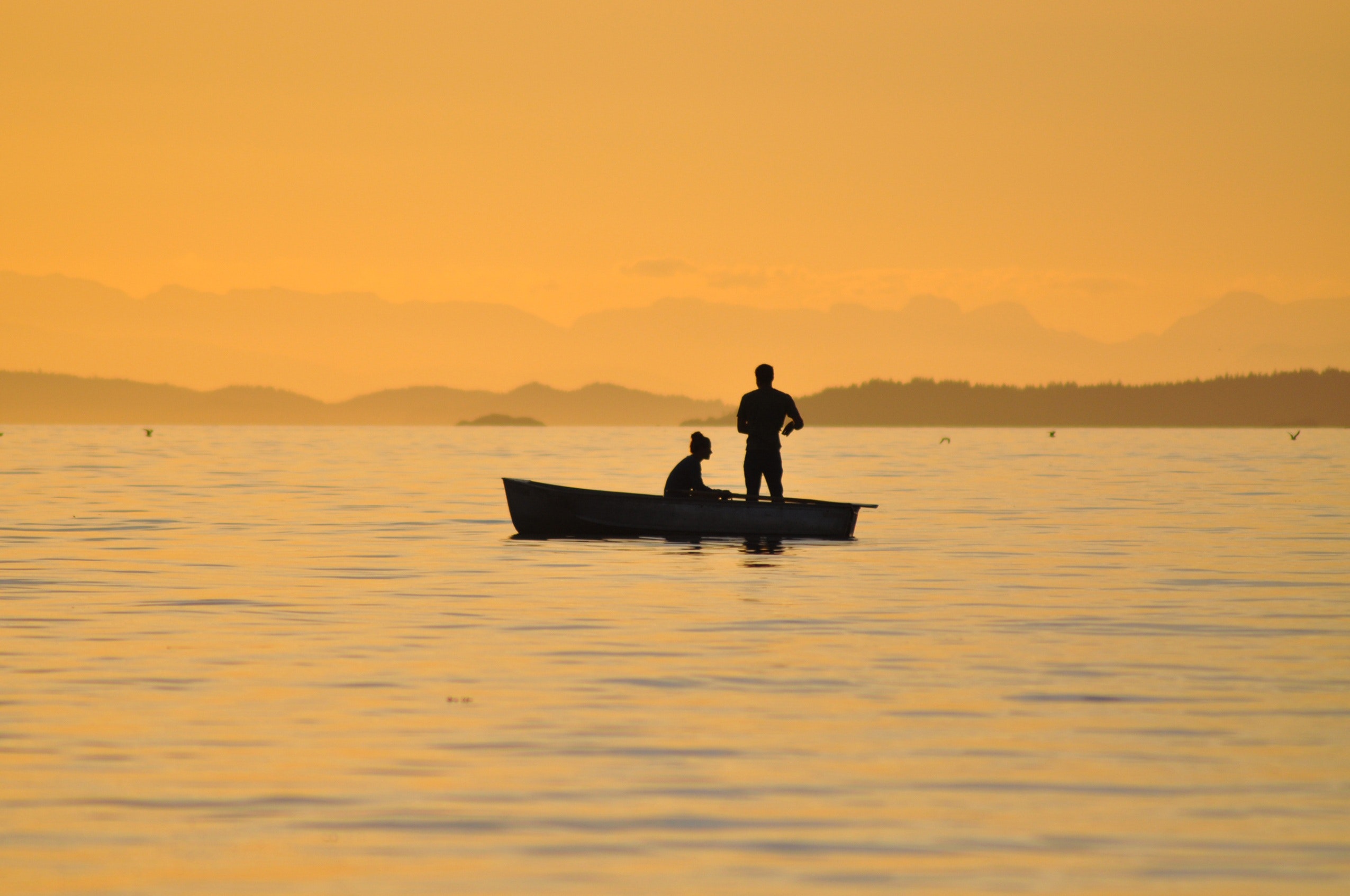 Two people in a boat on the water at sunset.