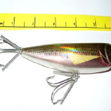 A small fishing lure next to a measuring tape.