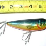 A fishing lure is next to a measuring tape.