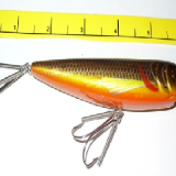A fishing lure is next to a measuring tape.
